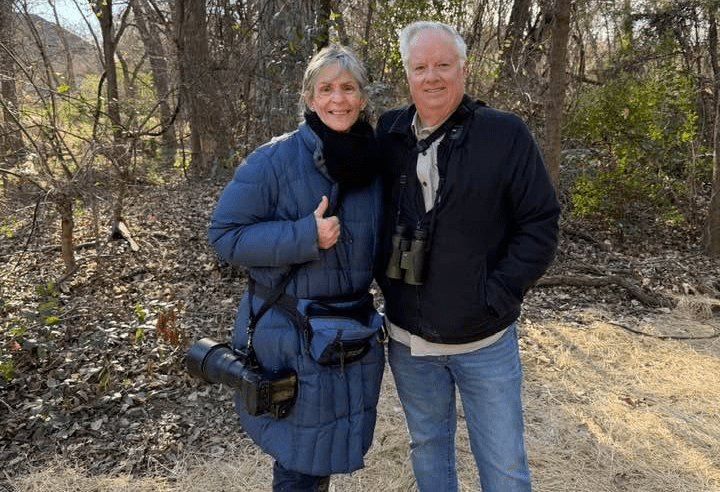 A couple posing outdoors with camera gear on a wooded trail.