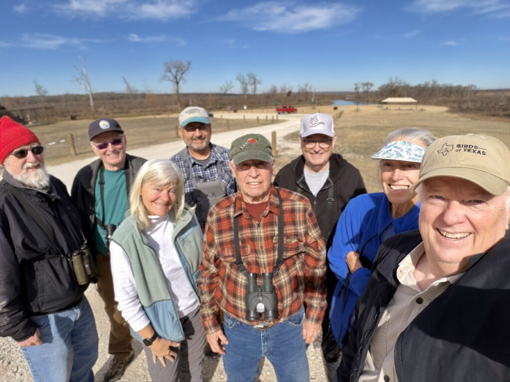Group of seven older adults smiling outdoors on a sunny day.